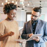 Photo of a man (holding a tablet) and a woman speaking in an office setting. / AI in B2B marketing