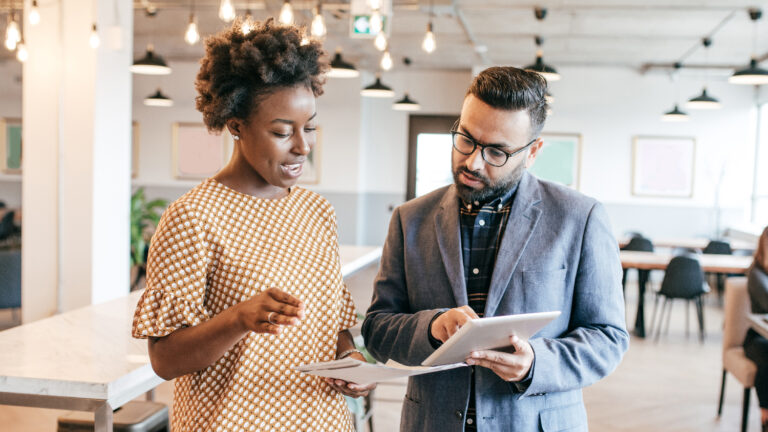 Photo of a man (holding a tablet) and a woman speaking in an office setting. / AI in B2B marketing