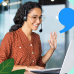 A smiling saleswoman waves while using a laptop from the deal desk.